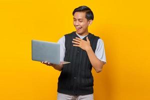 retrato de homem asiático animado segurando laptop sobre fundo amarelo foto