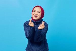 mulher asiática jovem e alegre mostrando o sinal do coração com os dedos cruzados sobre um fundo azul