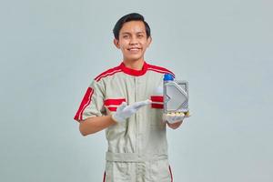 retrato de homem bonito sorridente, vestindo uniforme de mecânico, mostrando a garrafa de plástico de óleo de motor sobre fundo cinza foto