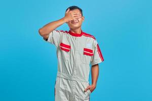 retrato de um jovem mecânico asiático cobrindo o rosto com as palmas das mãos sobre fundo azul