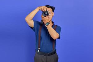 retrato de um jovem asiático bonito segurando uma câmera profissional e pronto para tirar uma foto em fundo roxo