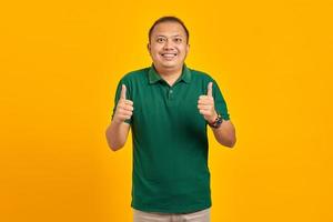 jovem asiático bonito alegre mostrando gesto de polegar para cima isolado em fundo amarelo