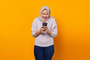 retrato de mulher asiática atraente e alegre usando telefone celular sobre fundo amarelo
