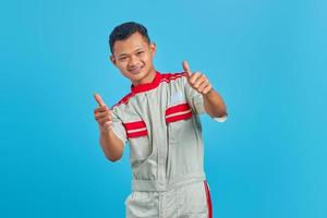 retrato de animado jovem mecânico asiático mostrando gesto de polegar para cima isolado sobre fundo azul foto