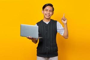 Feliz jovem bonito empresário tendo uma ideia criativa enquanto segura um laptop sobre fundo amarelo