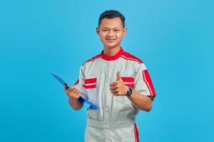 retrato de um jovem mecânico asiático animado segurando a prancheta e mostrando o polegar para cima gesto isolado sobre fundo azul foto