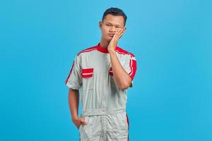retrato de um jovem mecânico asiático tocando a boca com uma expressão dolorida sobre um fundo azul