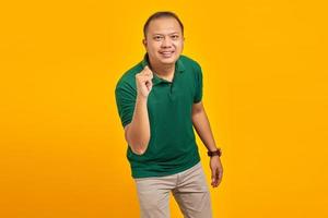 retrato de homem asiático mostrando gesto de mão dobrando os dedos na frente da câmera com uma expressão engraçada sobre fundo amarelo foto