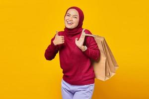 linda mulher asiática segurando sacolas de compras e mostrando os polegares com uma cara sorridente foto