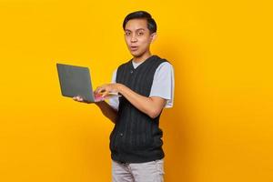 alegre bonito jovem empresário segurando um laptop e olhando para a câmera em fundo amarelo foto