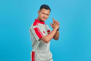 retrato de um jovem mecânico asiático segurando uma arma simbólica com um gesto de mão sobre o fundo azul