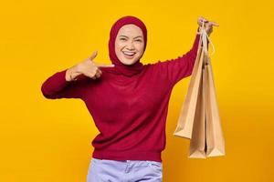linda mulher asiática mostrando algumas sacolas de compras e dando os polegares para cima com uma cara sorridente no fundo amarelo
