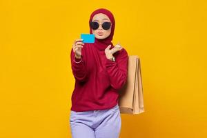 jovem mulher asiática sorridente segurando sacolas de compras e cartão de crédito em fundo amarelo
