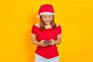 retrato de uma jovem sorridente com chapéu de Natal enviando mensagem no smartphone em fundo amarelo