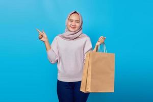 retrato de uma mulher asiática alegre segurando uma sacola de compras e apontando o dedo para o espaço vazio foto