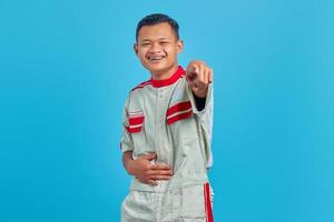 retrato de um jovem mecânico asiático, mostrando uma gargalhada com a mão na barriga e o dedo apontando para a câmera sobre fundo azul