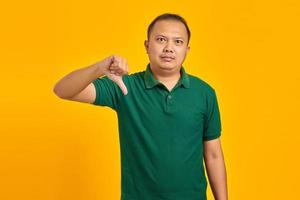 jovem asiático com raiva mostrando rejeição com gesto de polegar para baixo sobre fundo amarelo foto