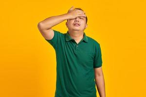 jovem asiático frustrado segurando um rosto com uma mão sobre fundo amarelo