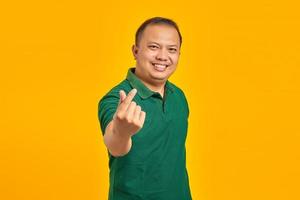 retrato de um jovem asiático sorridente, mostrando o coração do dedo sobre fundo amarelo
