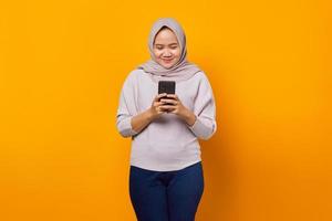 retrato de mulher asiática atraente e alegre usando telefone celular sobre fundo amarelo