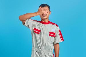 retrato de um jovem mecânico asiático cobrindo o rosto com as palmas das mãos sobre fundo azul