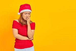 jovem asiática com chapéu de Natal, parecendo estressada e nervosa, com a mão na boca roendo as unhas