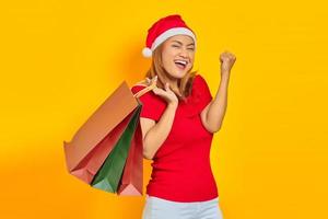 jovem alegre com chapéu de Papai Noel segurando sacolas de compras e comemorando a satisfação das compras foto
