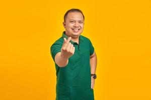 retrato de um jovem asiático sorridente, mostrando o coração do dedo sobre fundo amarelo