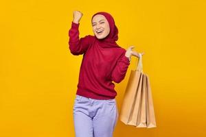 Mulher asiática animada comemorando o sucesso com uma expressão sorridente e mostrando sacolas de compras sobre fundo amarelo