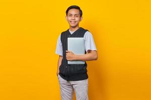 retrato de homem asiático sorridente traz laptop sobre fundo amarelo