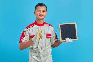 retrato de um jovem mecânico asiático alegre segurando uma placa em branco e fazendo um gesto de ok sobre o fundo azul
