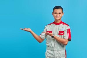 retrato de um jovem mecânico asiático sorridente, apontando para um espaço vazio isolado em um fundo azul foto