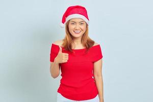 retrato de uma bela mulher asiática sorridente usando vestido de Natal e mostrando os polegares para cima ou sinal de aprovação em fundo branco foto