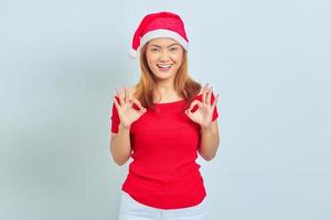 retrato de uma linda mulher asiática sorridente usando vestido de Natal e mostrando gesticulando sinal de tudo bem no fundo branco foto