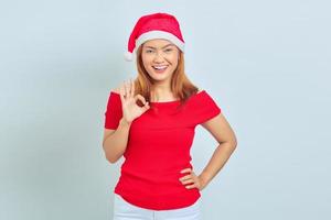 retrato de uma linda alegre mulher asiática com vestido de Natal e mostrando um gesto de ok no fundo branco foto