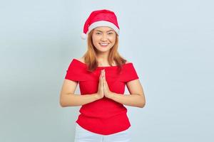 jovem asiática sorridente com chapéu de Natal de mãos dadas e se sentindo otimista sobre um fundo branco foto