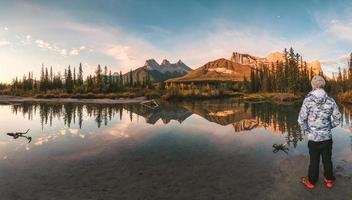 homem viajante em pé apreciar a paisagem de três irmãs montanhas reflexo no rio no outono pela manhã foto