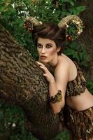 garota com chifres trançados em um vestido feito de casca de árvore em uma floresta foto