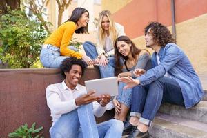 grupo multiétnico de jovens olhando para um tablet digital ao ar livre em meio urbano.