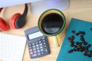 a mesa de trabalho tem uma xícara de café, fones de ouvido vermelhos e suprimentos de escritório. foto