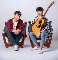 dois jovens sentados em uma cadeira segurando um violão foto