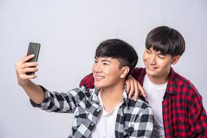 dois amáveis jovens se sentam em uma cadeira e tiram uma selfie em um smartphone.
