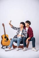 dois amáveis jovens se sentam em uma cadeira e tiram uma selfie em um smartphone. foto