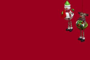 brinquedos de Natal pendurados isolados em um boneco de neve de fundo vermelho e cervos da neve. conceito de cartão de felicitações de ano novo, convite e embalagem foto