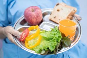 paciente asiático sênior ou idosa idosa comendo alimentos saudáveis de vegetais de café da manhã com esperança e feliz enquanto está sentado e com fome na cama no hospital. foto