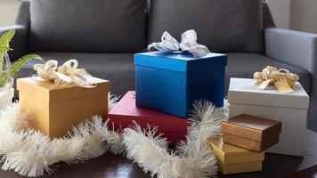 lindas caixas de presente de natal embrulhadas em papel colorido com laço de fita na mesa da sala de estar de casa foto