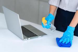 mulher de negócios usando máscara e usando desinfetante pessoal para limpar a mesa no escritório para manter a higiene. preventiva durante o período de epidemia de coronavírus ou covid19. foto