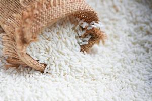 arroz branco de jasmim no saco e arroz colhido na mesa de madeira, conceito de cozimento de grãos de arroz e alimentos foto