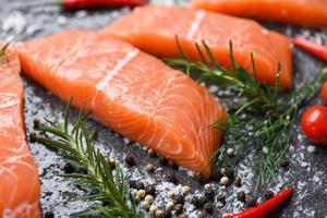 filé de salmão cru com ervas e especiarias em fundo preto escuro foto