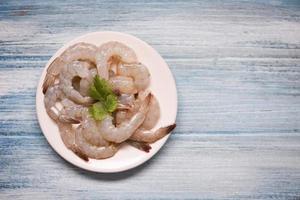 camarões frescos ou camarões, frutos do mar prateados - camarão cru na chapa branca e fundo de madeira para cozinhar foto